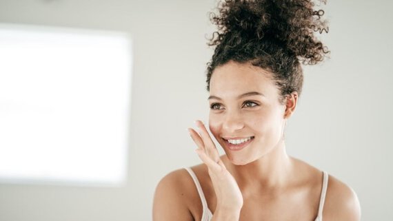 A woman with a joyful expression, gently touching her face with her hand, radiating happiness.